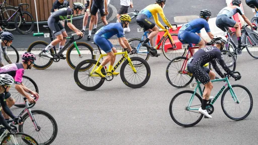 Des cyclistes en tenue de compétition participent à une course sur route urbaine, chacun sur un vélo de piste coloré, sans freins ni dérailleur, typique des critériums.